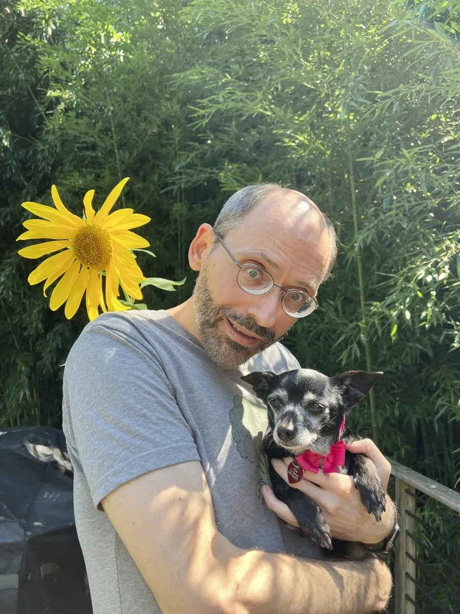 Dr Greger holding his dog beside a sunflower