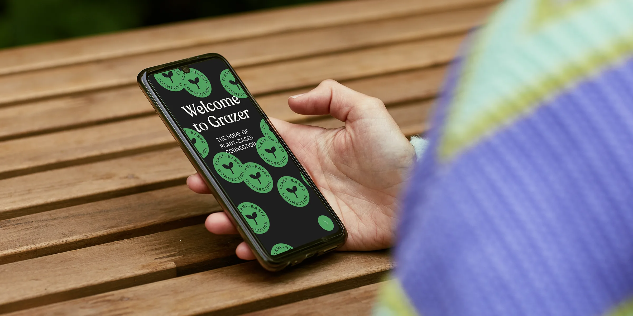 A hand holding a phone open on Grazer's welcome screen: Welcome to Grazer, the home of plant-based connection